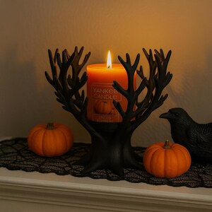 May include: An orange Yankee Candle, lit, is in a black tree-shaped holder. Two small orange pumpkins and a black crow figurine are on display. The candle label reads "Spiced Pumpkin."