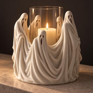 Peut inclure: Un bougeoir circulaire composé d'un cercle de silhouettes de fantômes blanc cassé aux textures de tissu drapé. Un cylindre en verre transparent est placé au centre, contenant une bougie pilier crème allumée avec une flamme jaune chaude.