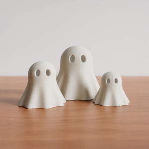 Könnte beinhalten: Drei weiße Geisterfiguren in verschiedenen Größen, jede mit zwei ovalen Augenausschnitten. Die Geister haben ein einfaches, drapiertes Design und sind auf einer Holzoberfläche angeordnet. Der Hintergrund ist hell.