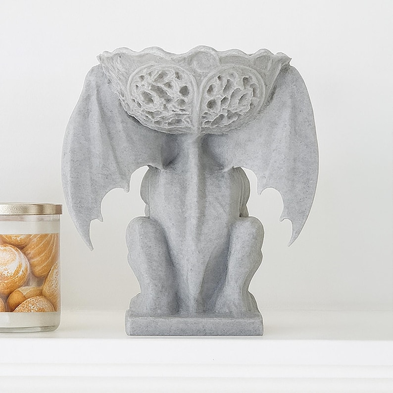 Pode incluir: Est&aacute;tua de g&aacute;rgula cinzenta com asas abertas e um topo em forma de tigela. A est&aacute;tua &eacute; detalhada com padr&otilde;es esculpidos e assenta numa base retangular. Um item decorativo para interiores ou exteriores.