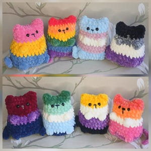 May include: Eight plush cat-shaped toys made of chunky yarn, each featuring a different colour pattern. The cats have small black button eyes and embroidered noses. The colours include pink, yellow, blue, red, orange, green, white, purple, and black.