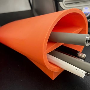 May include: Orange plastic desk organizer with three pens inside. The organizer is shaped like a cone and has a rounded opening at the top.