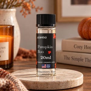 Può includere: Un flacone in vetro trasparente con tappo nero e un'etichetta nera con il testo Scentia, Pumpkin Boo, 20ml, Pumpkin, Cinnamon, Nutmeg, Made in USA e Discovery Size, decorato con piccole illustrazioni di foglie d'acero rosse.