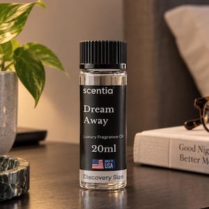 May include: A clear glass bottle of Scentia Dream Away luxury fragrance oil with a black ribbed cap. The black label features white text reading Dream Away, Luxury Fragrance Oil, 20ml, Discovery Size, and a small American flag icon with USA text.