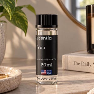 Può includere: Un flacone in vetro trasparente di olio profumato di lusso Scentia You con tappo nero a coste. L'etichetta nera riporta il testo bianco Scentia, You, Luxury Fragrance Oil, 20ml, Discovery Size e un'icona della bandiera americana con la scritta USA.