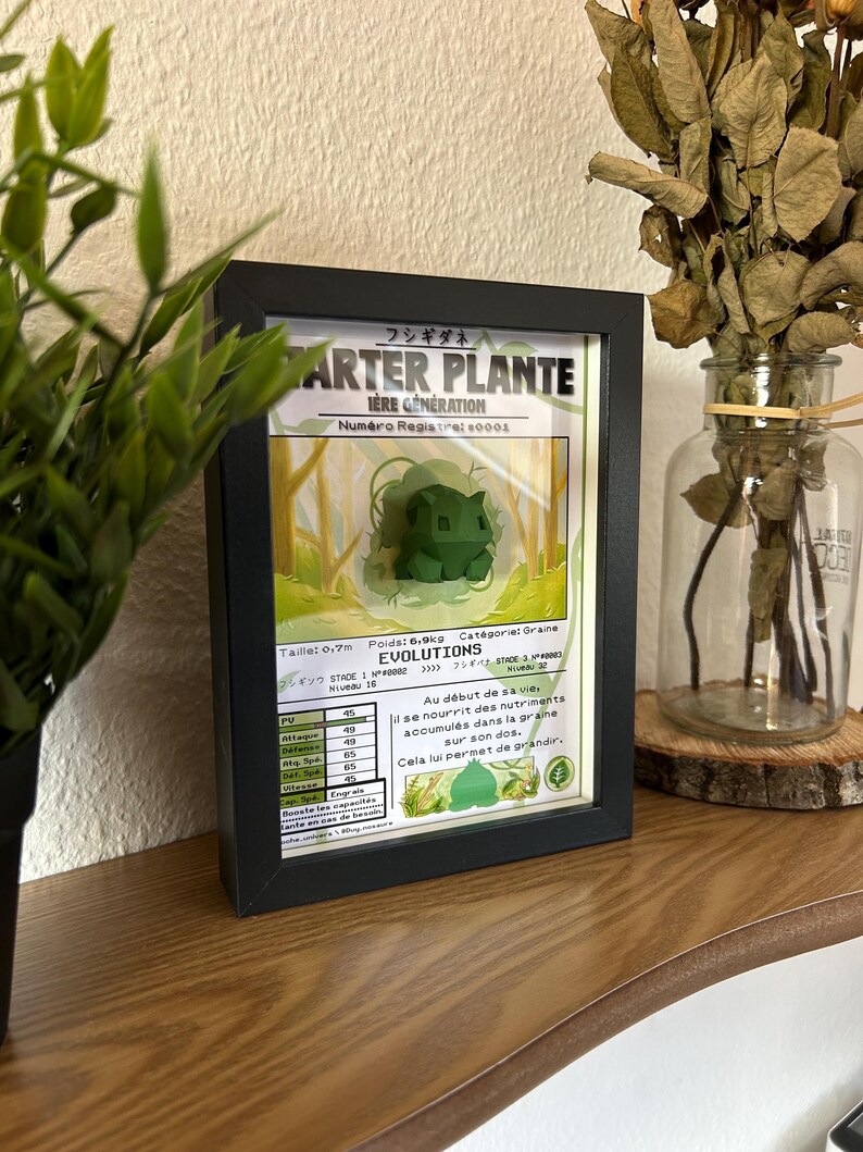 Op de afbeelding: Een ingelijste Pok&eacute;mon-kaart met Bulbasaur, de Grass-type starter Pok&eacute;mon uit de eerste generatie. De kaart is in het Frans en bevat informatie over Bulbasaur's statistieken, evolutie en vaardigheden. De kaart wordt weergegeven tegen een houten achtergrond.