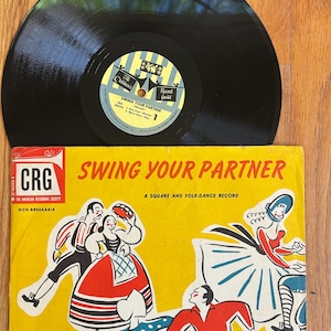 May include: A vintage vinyl record and album cover. The album cover is yellow with the title "SWING YOUR PARTNER" and illustrations of dancers. The record is black and shiny, with a label that reads "Swing Your Partner".