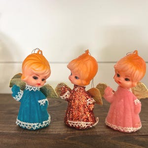 May include: Three vintage angel ornaments with orange hair, gold wings, and detailed faces. One is teal, one is glittery red-orange, and one is pink. Each has a white lace trim.