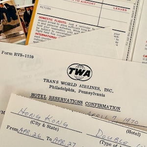 May include: A collection of vintage Trans World Airlines (TWA) documents including a hotel reservation confirmation form dated April 7, 1970, for Hong Kong, alongside a baggage claim ticket and informational pamphlets with black text on white paper.