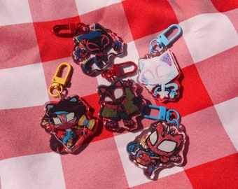Puede incluir: Cinco llaveros coloridos con personajes de dibujos animados con detalles rojos, blancos y negros. Los llaveros están hechos de acrílico transparente y tienen anillos metálicos para sujetarlos a llaves o bolsos.