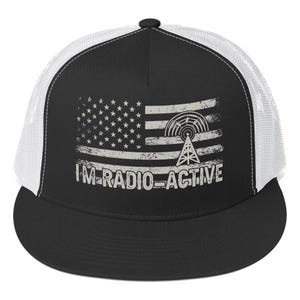 May include: Black and white trucker hat with a white mesh back. The front panel features a distressed American flag design with a radio tower graphic and the text "I'M RADIO-ACTIVE".