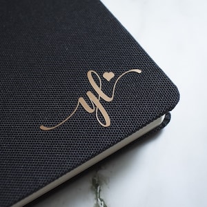 May include: A black notebook with a gold foil inscription that reads "yfl" with a small heart above the "l".