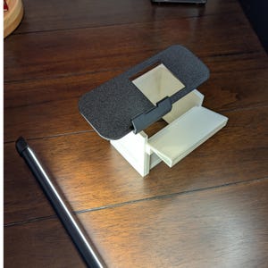 K&ouml;nnte beinhalten: Ein wei&szlig;es 3D-gedrucktes Modell eines kleinen Hauses mit einem schwarzen Deckel, der sich &ouml;ffnen l&auml;sst. Der Deckel hat eine strukturierte Oberfl&auml;che und eine rechteckige &Ouml;ffnung.