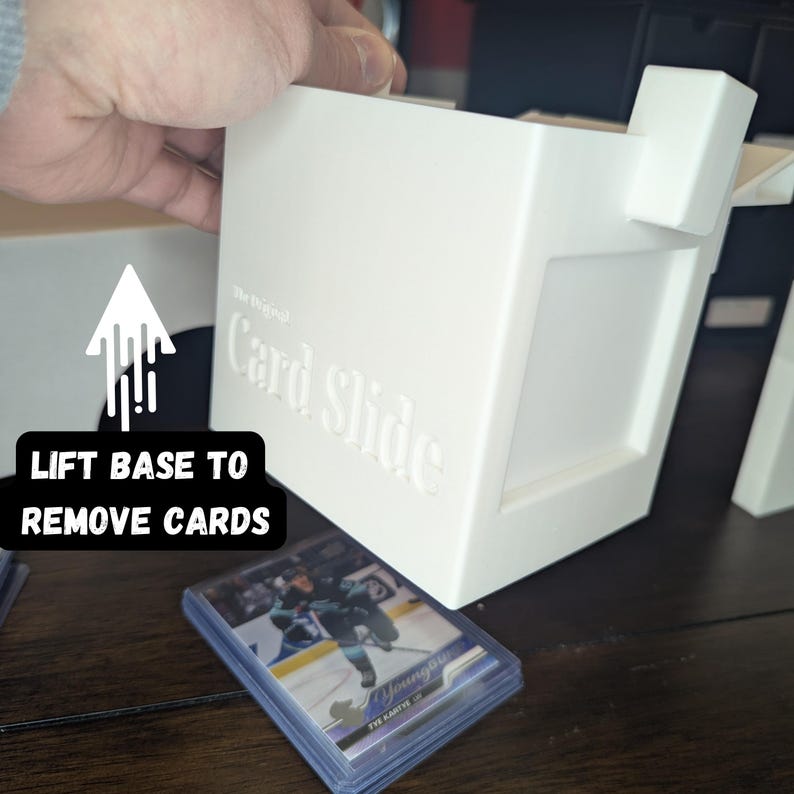 K&ouml;nnte beinhalten: Wei&szlig;e Plastik-Kartenaufbewahrungsbox mit dem Text "The Original Card Slide" in Pr&auml;gung an der Seite. Die Box ist ge&ouml;ffnet und ein Stapel Sammelkarten ist darunter sichtbar.