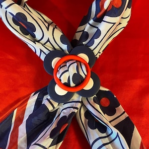 May include: A blue and white patterned scarf with red flowers. The scarf is tied in a knot and has a large, red and white flower-shaped clasp.
