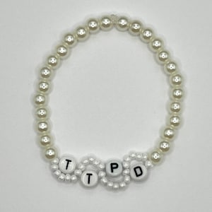 May include: White pearl bracelet with the letters "TTPD" spelled out in black on white beads.