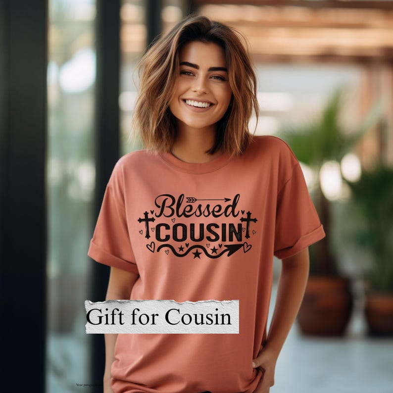May include: A coral-colored t-shirt with the words "Blessed Cousin" in black script and a decorative design. The shirt also has the text "Gift for Cousin" in a white rectangle.