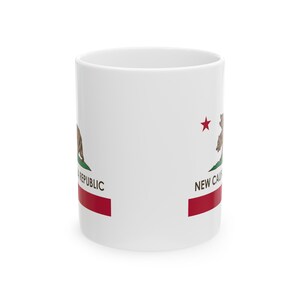 May include: White ceramic mug featuring the California Republic flag design. The flag includes a brown bear, green grass, a red star, and a red stripe at the bottom. The words "NEW CAL" and "REPUBLIC" are also visible.