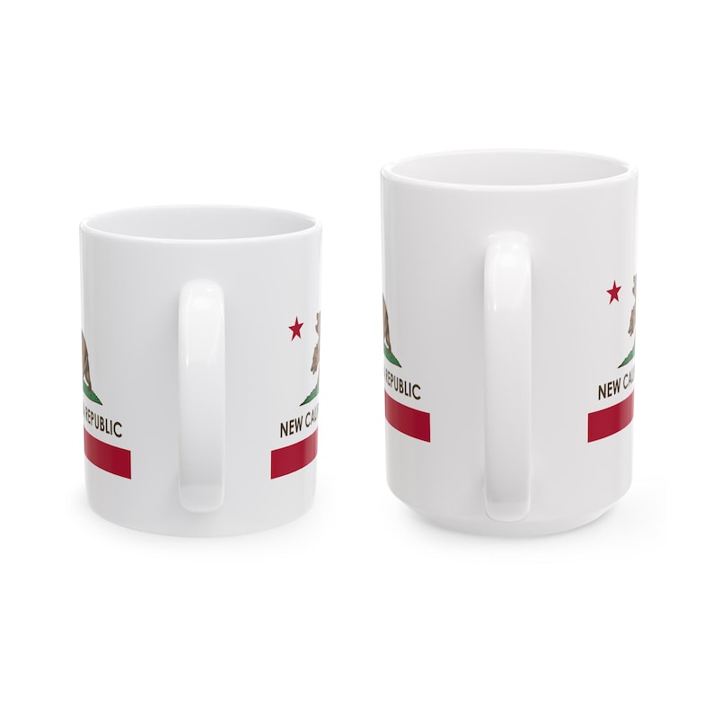 May include: Two white ceramic mugs with the New California Republic flag design. The design includes a bear, a red stripe, a red star, and the words "NEW CAL REPUBLIC". The mugs have white handles.