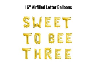 May include: Gold air-filled letter balloons spelling "SWEET TO BEE THREE". Each balloon is approximately 16 inches tall. The balloons are arranged on a white background, perfect for a birthday celebration.