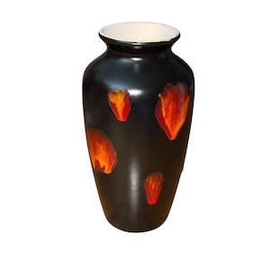 Op de afbeelding: Een zwarte keramische vaas met een witte binnenrand en een glanzende afwerking. De vaas heeft abstracte, bloembladachtige ontwerpen in rood en oranje. De vaas is een decoratief item voor in huis.