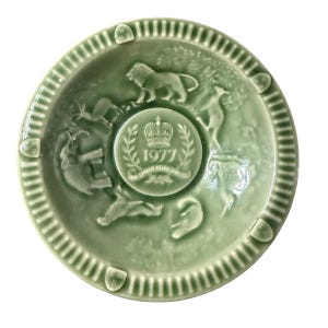 May include: A green ceramic commemorative dish with embossed images of animals and text. The center features a crown and the year 1977, with the words "The Queen's Silver Jubilee". The rim has a ribbed design.
