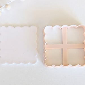 May include: Two plastic cookie cutters, one with a scalloped edge and the other with a scalloped edge and a divided interior. Both are light pink in color.