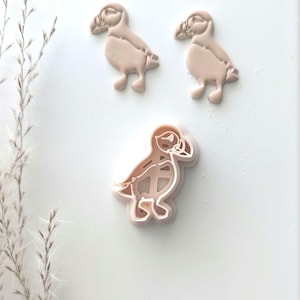 May include: Three plastic cookie cutters shaped like puffins. The cutters are a light pink color.