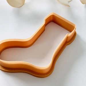 May include: A light brown plastic cookie cutter shaped like a stocking.