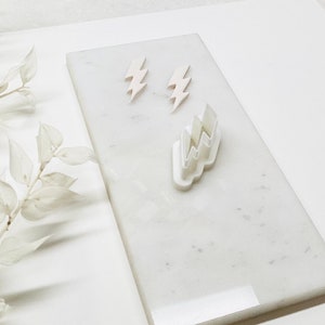 May include: White marble surface with three white lightning bolt shaped cookie cutters. Two of the cutters are small and one is larger.