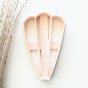 May include: A pink plastic cookie cutter shaped like a fan with a decorative design.