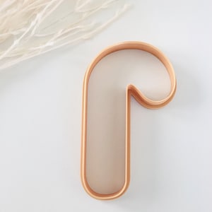May include: A wooden candy cane cookie cutter. The cutter is a light brown colour and has a smooth surface.