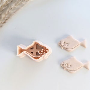 May include: Three cookie cutters in the shape of a fish. The cutters are made of a light pink plastic. The largest cutter is open and the two smaller cutters are closed.