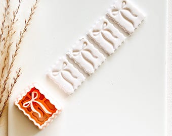 Peut inclure: Vue aérienne de plusieurs biscuits décoratifs. Un biscuit est rectangulaire avec un motif de nœud orange et blanc. Il y a cinq biscuits blancs avec un motif de nœud. Les biscuits sont sur une surface blanche.