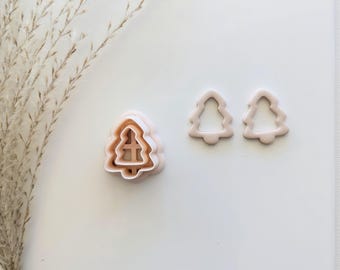 May include: Three pink plastic Christmas tree cookie cutters. The largest cutter is in the centre of the image and is stacked on top of two smaller cutters. The two smaller cutters are to the right of the image.