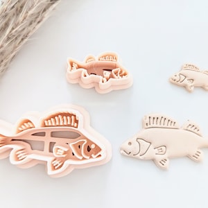 Puede incluir: Tres cortadores de galletas de plástico rosa con forma de pez. El cortador más grande es de doble capa, el mediano es de una sola capa y el más pequeño es de una sola capa.