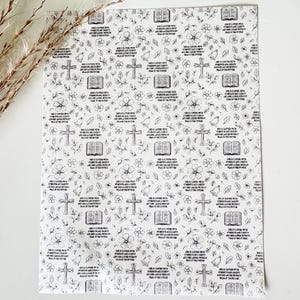 May include: A rectangular sheet of white paper featuring a repeating black line art pattern of open books, crosses, bells, and flowers. The text "She is clothed with strength and dignity and she laughs without fear of the future" is printed repeatedly.