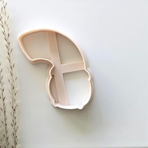 May include: A white plastic cookie cutter shaped like a banana with a cross-hatch pattern.