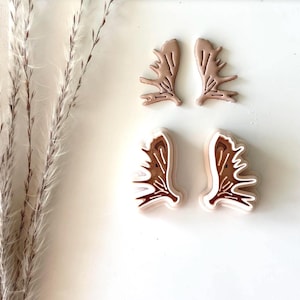 May include: Four brown plastic cookie cutters shaped like moose antlers. The cutters are on a white surface.