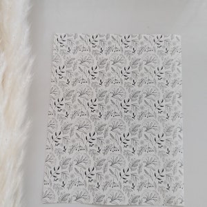 May include: White sheet of paper with a black and white floral pattern. The pattern features small leaves and flowers.