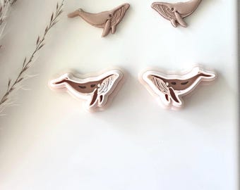 May include: Four whale-shaped cookie cutters, two large and two small. The cutters are made of a light brown plastic and are arranged on a white background.