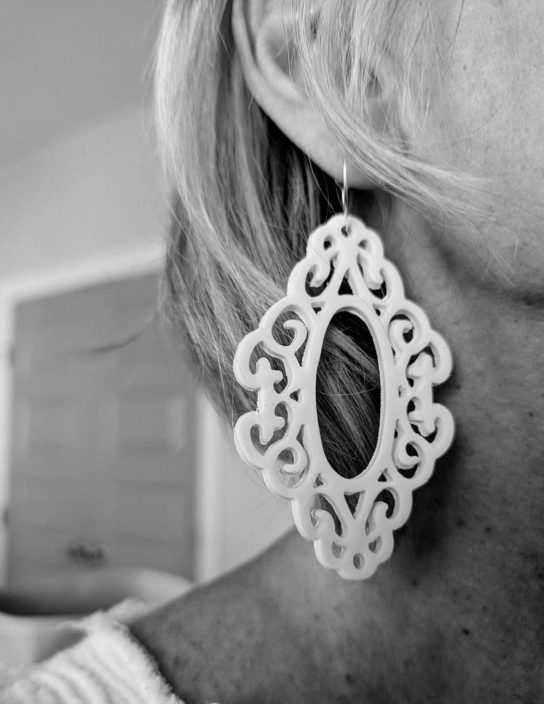 May include: White filigree earrings with a large oval cutout in the center. The earrings are made of a lightweight material and have a delicate, feminine design.