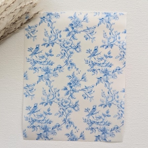 May include: A white fabric with a blue floral pattern featuring small birds. The pattern is a repeating design of flowers and branches with birds perched on the branches.