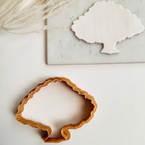 May include: A brown plastic cookie cutter shaped like a tree. The cutter has a detailed, wavy edge around the top and a smooth, rounded bottom.