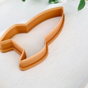 May include: A brown plastic cookie cutter shaped like a rocket ship.