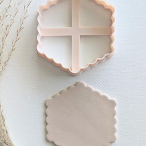 May include: A pink plastic cookie cutter in the shape of a scalloped rectangle. A light pink clay cutout is next to the cutter.