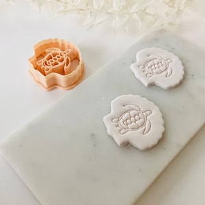 May include: Two white fondant turtle shapes with a raised design, and a plastic turtle cookie cutter.