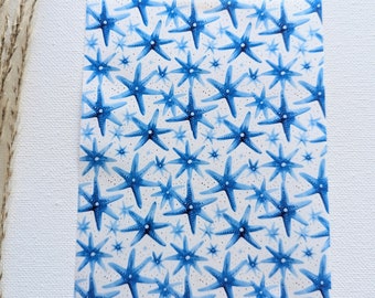 Può includere: Uno sfondo bianco con un motivo ripetitivo di stelle marine blu ad acquerello. Le stelle marine sono di dimensioni diverse e hanno un aspetto maculato.
