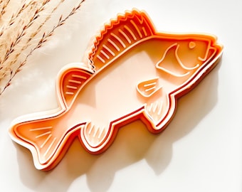 Può includere: Un tagliabiscotti a forma di pesce color salmone con un contorno bianco. Il tagliabiscotti presenta pinne e squame dettagliate, perfetto per creare biscotti o decorazioni in fondente a tema pesce. Il tagliabiscotti è realizzato in plastica resistente.