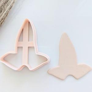 May include: A pink plastic cookie cutter in the shape of a witch's hat. The cutter is shown next to a piece of pink fondant that has been cut out using the cutter.
